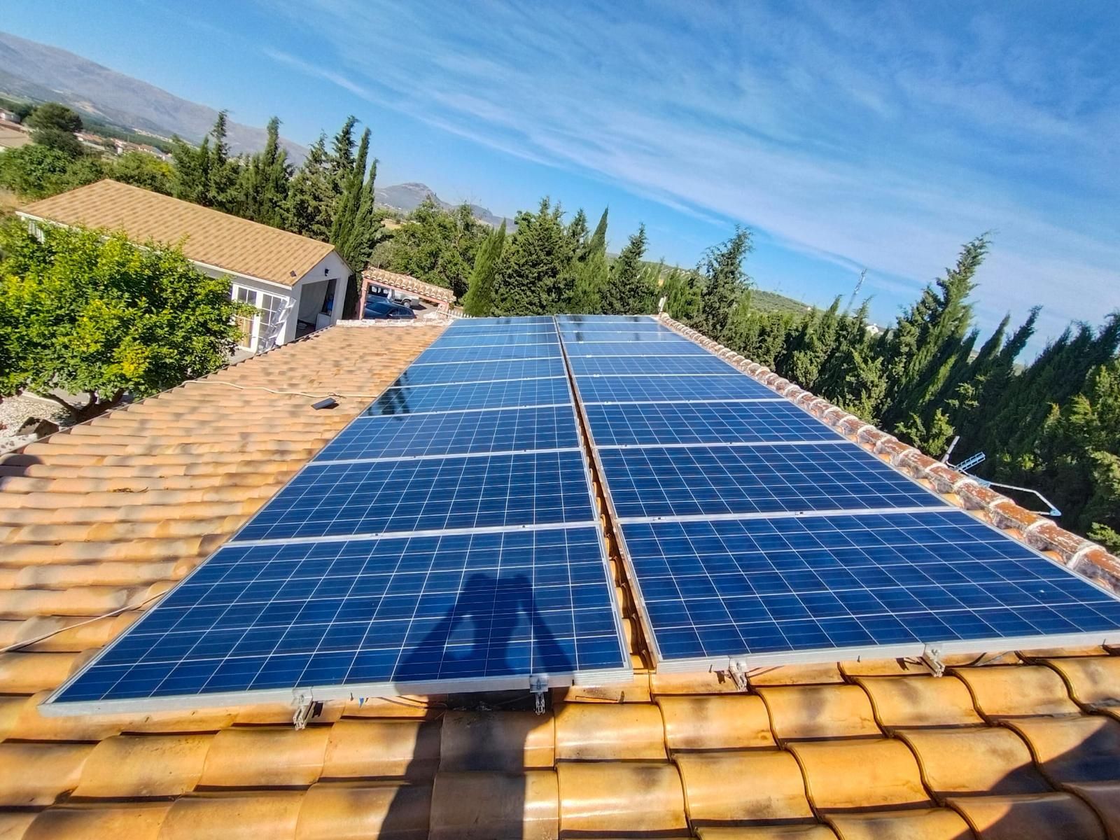 Dos filas de paneles solares sobre un tejado de teja en un entorno arbolado